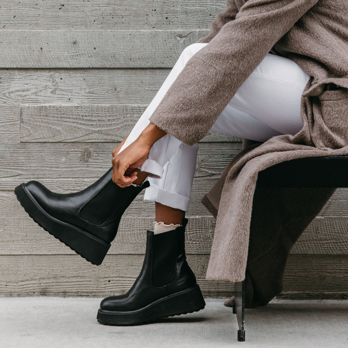 Heyday All Black Platform Chelsea Boot in black, lifestyle view worn with white trousers while seated.