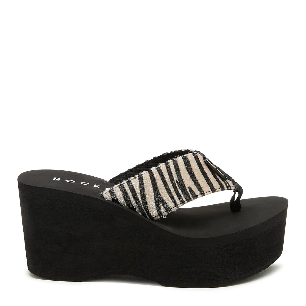 Side view of the Rocket Dog Crush tan animal print flip flop, animal print strap on a black wedge platform